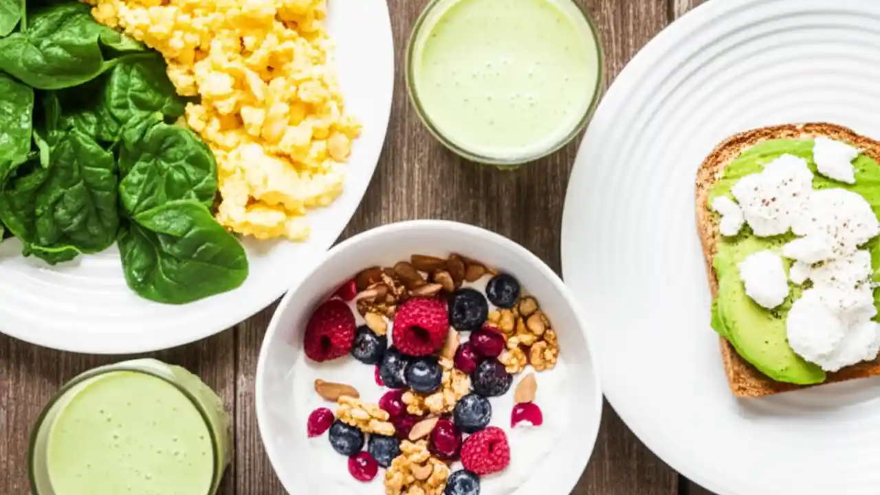 A top-down view of a colorful high-protein breakfast spread featuring yogurt, eggs, smoothie, and toast on a wooden table, emphasizing healthy eating.