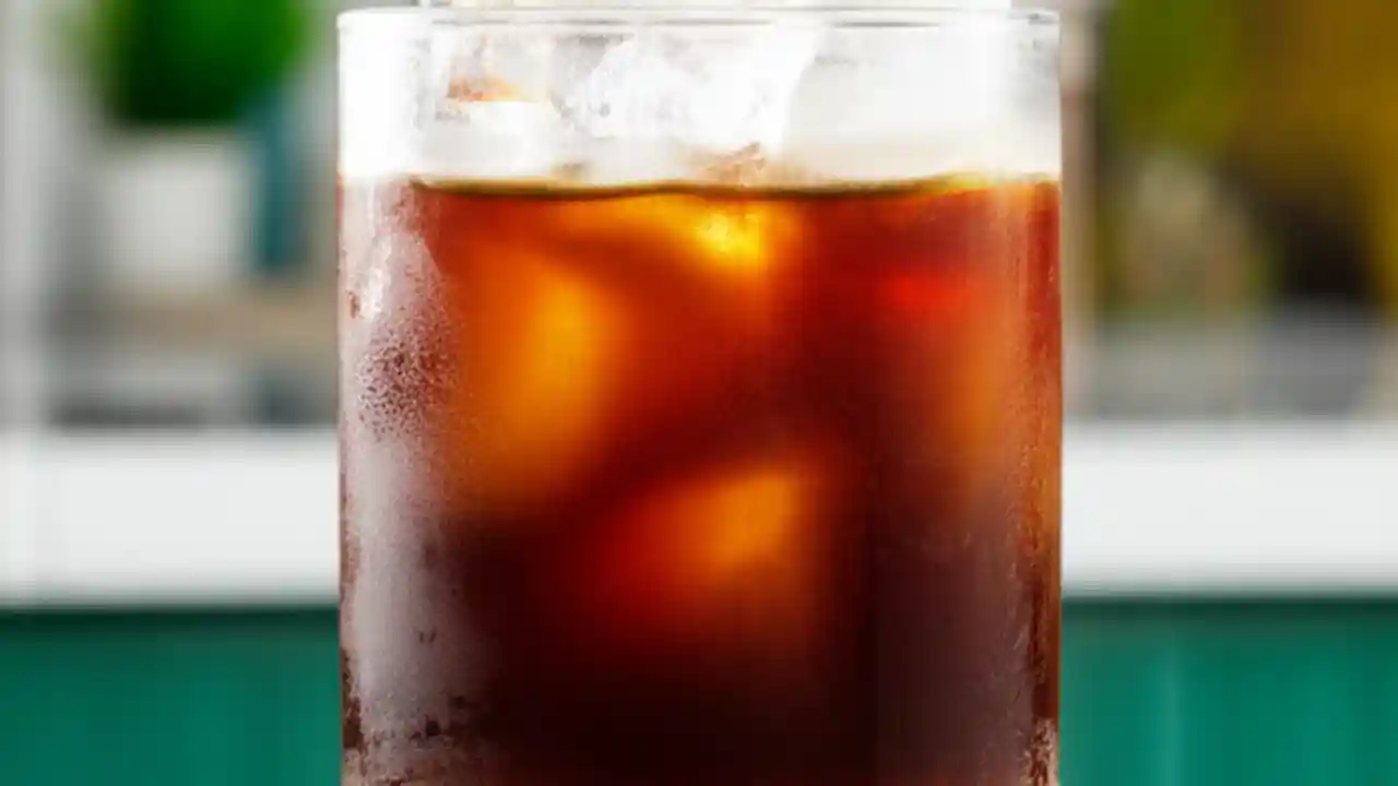 A tall glass of perfectly layered homemade iced coffee with cold brew, milk, and large ice cubes, set in a bright, modern kitchen.
