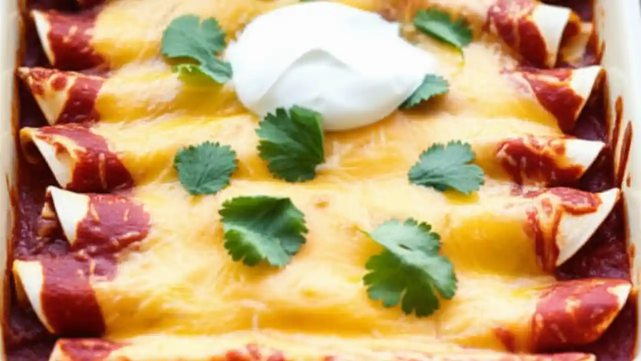A close-up of cheesy, bubbling vegetarian enchiladas in a baking dish, garnished with fresh cilantro and sour cream.